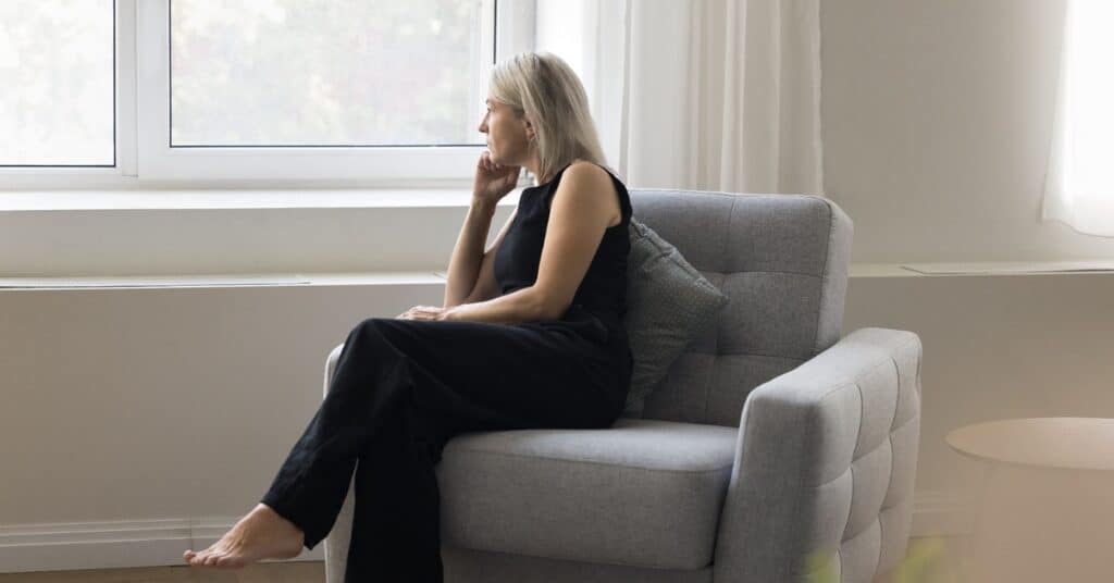 Woman sitting thoughtfully by a window, reflecting on early signs of perimenopause